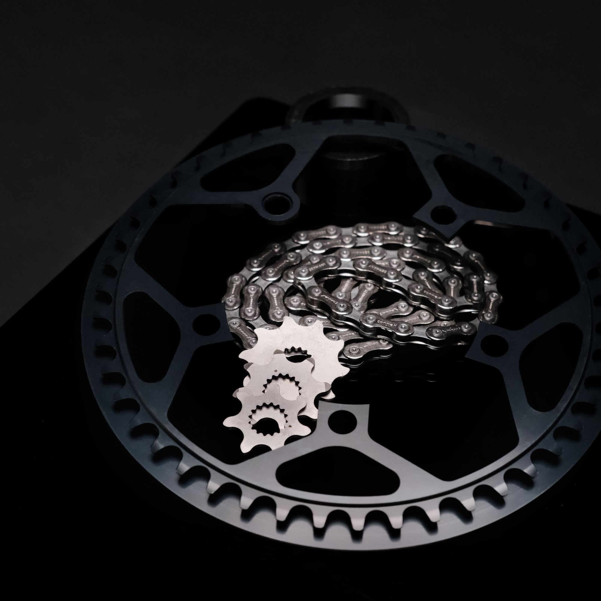 chainring, three sprockets and a chain on a black plate